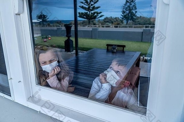 2019冠状病毒疾病在家隔离期间，戴着口罩的悲伤儿童透过窗户看。<strong>学校</strong>关门时，孩子们感到悲伤。科罗纳维鲁