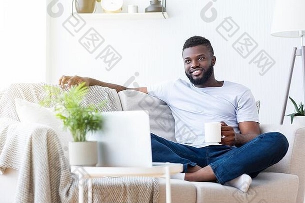 轻松的非洲小伙子在笔记本电脑上享受早晨新闻
