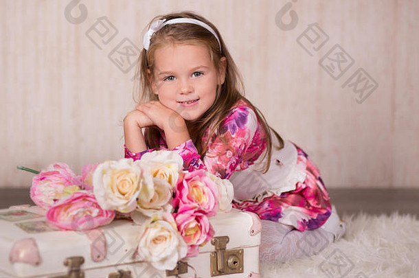 可爱的小女孩，深色头发，粉红色的脸颊，绿色的眼睛，穿着色彩鲜艳的裙子和花哨的休闲鞋坐在摄影棚里拍照