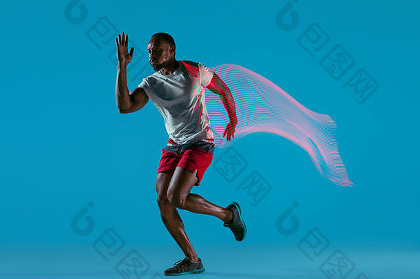 活跃的年轻非洲肌肉男跑步者的全长肖像，在蓝色工作室背景上与闪光灯隔离