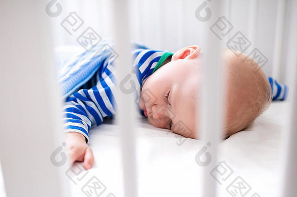 睡在白色婴儿床上的婴儿和他的玩具。托儿所内部和儿童床上用品。可爱的小男孩在摇篮里打盹。