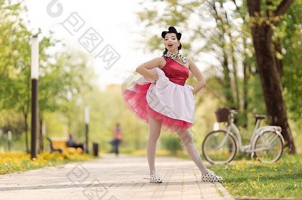 阳光明媚的日子里，一个穿着粉色连衣裙、留着40-50年代发型的美丽女孩在公园里跳舞、摆姿势。复古风格的照片。