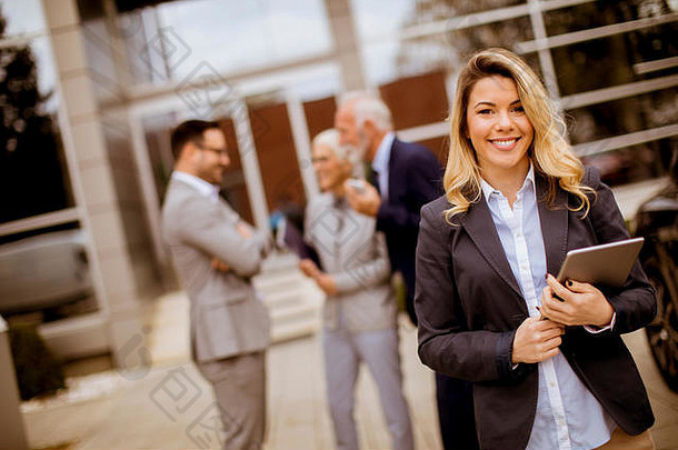 年轻的业务员站在户外，手里拿着文件，而其他业务人员则在后台交谈