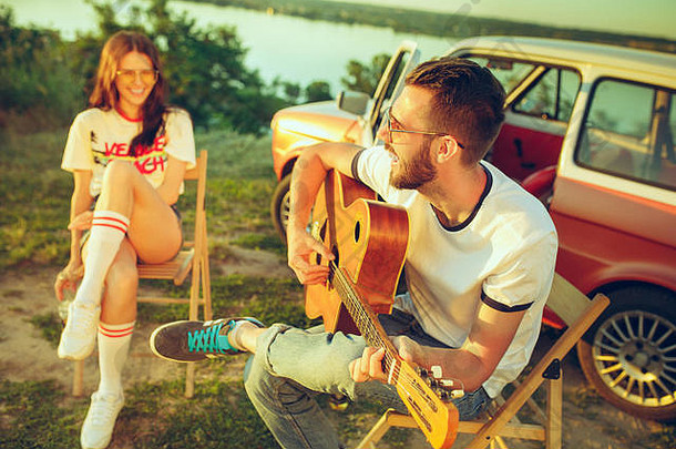 这对情侣在河边的一个夏日里坐在沙滩上弹吉他休息