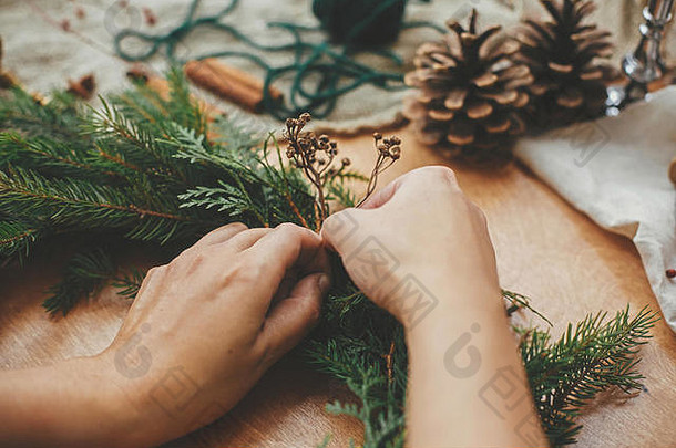 手拿着药草和冷杉枝、松果、线、浆果、肉桂放在木桌上。圣诞花圈工作坊。真实<strong>时尚</strong>的静物画。