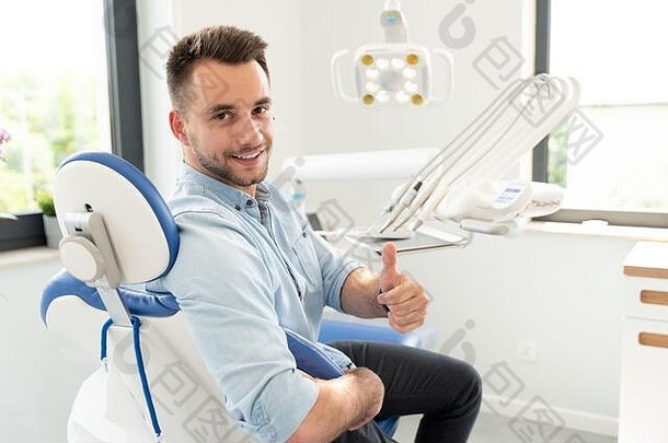 帅哥竖起大拇指，微笑着坐在牙科椅旁。专业牙科诊所，<strong>健康</strong>牙齿理念。