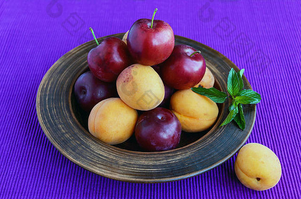 成熟的李子（品种：绿梅）和杏子放在一个粘土碗中，背景为明亮的紫色