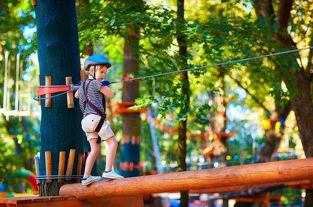 小男孩在高高的树丛中通过电缆线路，在冒险公园进行极限运动