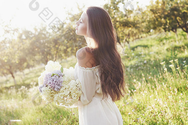 美丽的年轻的女孩白色光衣服花束夏天花了细一天花园