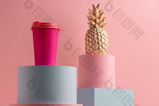 明亮的咖啡纸杯和粉红色背景上的金色菠萝