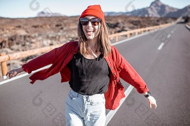 一位快活女人的肖像，穿着时髦的红色衬衫和帽子，在沙漠路上感到自由和快乐。无忧无虑的生活方式和旅游理念