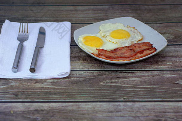 丰盛的早餐，塔雷尔卡与煎蛋和巴科诺站在一张木桌上，旁边是一张带刀叉的白色餐巾。