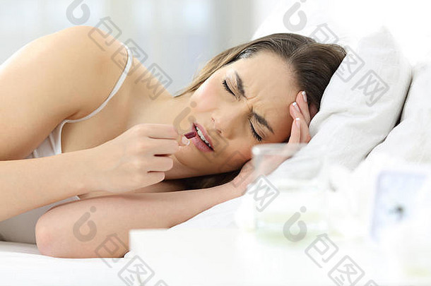 患有头痛的妇女在家里的床上服用止痛药
