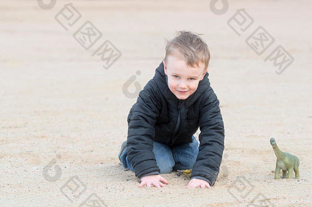 在凉爽的冬天，一个四岁的男孩和他的恐龙在沙滩上玩耍