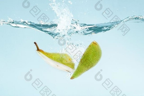 梨子切成两半，落在清澈的水中，溅在蓝色的背景上