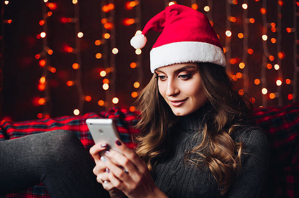 戴着红色<strong>圣诞</strong>帽的漂亮女人正在使用智能手机。