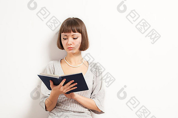 漂亮的年轻的女人阅读精装书书精益白色墙