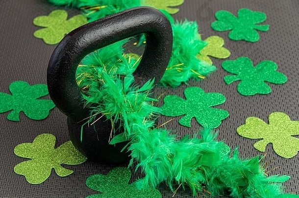 黑色健身房地板上的黑色铁壶铃和绿色羽毛蟒蛇，假日健身，绿色三叶草
