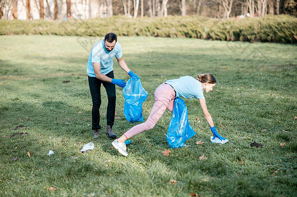 男人。女人志愿者穿着蓝色的t恤清洁公共花园塑料垃圾袋