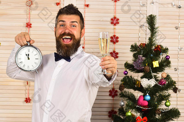 庆祝活动一年时间概念的家伙圣诞节树木墙背景男人。胡子持有玻璃香槟报警时钟聚会，派对男人。快乐的脸节日房间