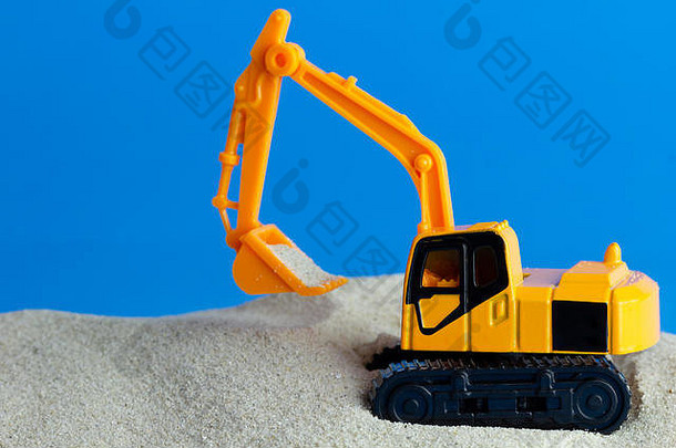 黄色的玩具反铲挖掘沙子蓝色的背景概念建设