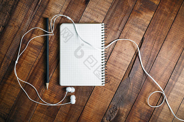 复古木桌背景上空白记事本、铅笔和耳机的照片