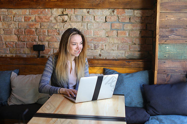 年轻的女人坐着舒适的咖啡房子表格玻璃杯卡布奇诺咖啡聊天移动PC