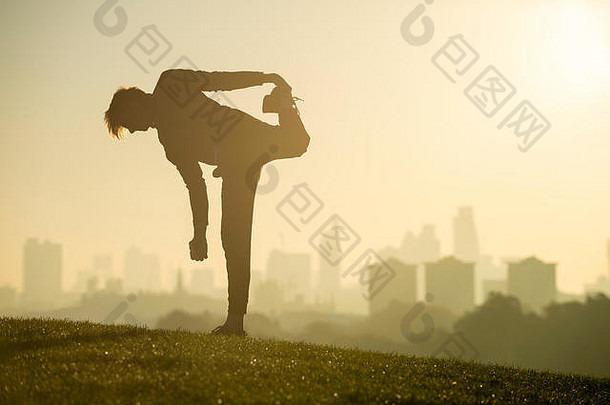 一个男人的剪影伸<strong>展</strong>在<strong>报</strong>春花山的草顶上，在伦敦天际线朦胧的金色日出前