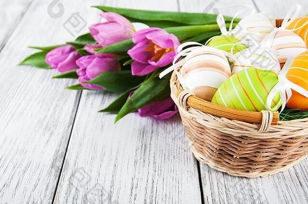 木桌上放着复活节彩蛋和郁金香的篮子