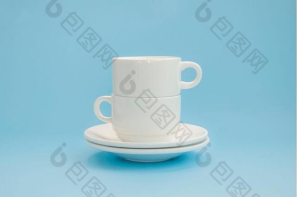 两个白色瓷杯和茶托，在浅蓝色背景上相互叠放。侧视图