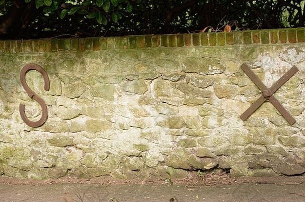 S..X由作为石墙支架的大型金属字母表示。环境中的字母。倾斜式挡土墙。