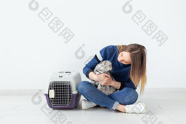 在一间新公寓的地板上，一位迷人、积极的年轻女子手里拿着一只漂亮的灰色折叠苏格兰猫。宠物概念。