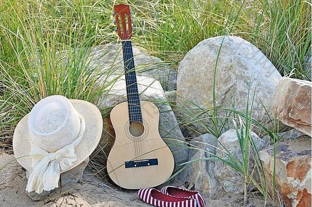 吉他，帽子，红白相间的条纹鞋，沙滩上的沙滩和岩石