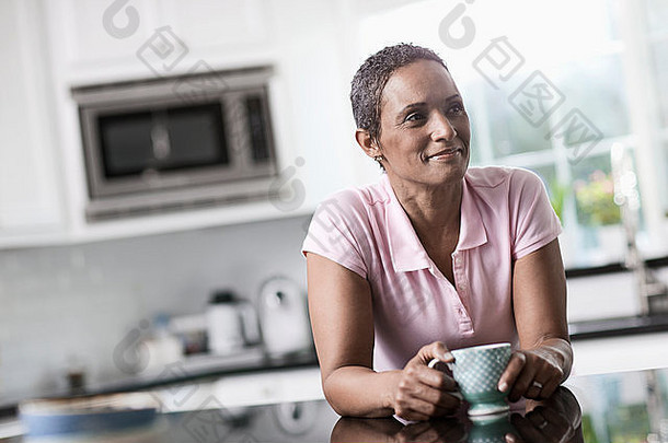 一位女士倚在厨房光滑的台面上，端着一杯咖啡。