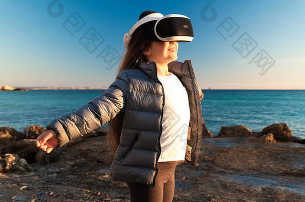 开心的女孩张开双臂，戴着3d虚拟现实耳机在海滩上。
