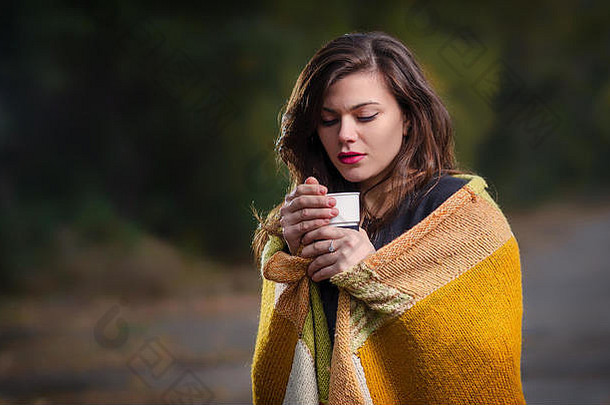 悲伤的女孩在户外端着一<strong>杯</strong>咖啡（茶），裹着一条温暖的毯子。