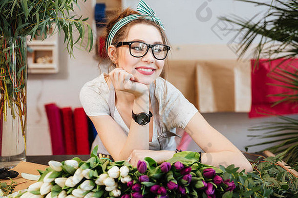 在花店工作的戴眼镜的迷人微笑的年轻女花商的肖像