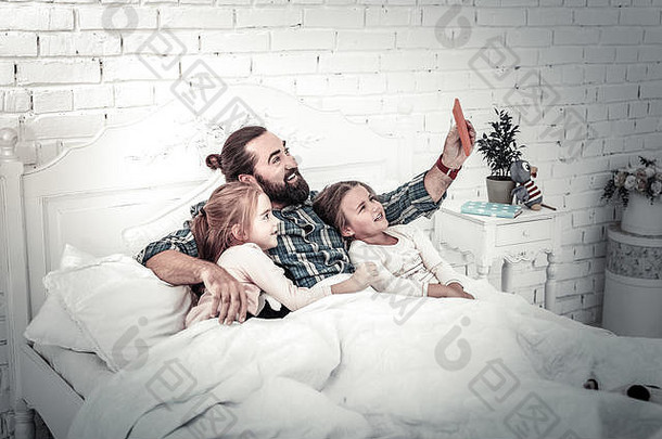 微笑的爸爸和两个孩子在床上自拍