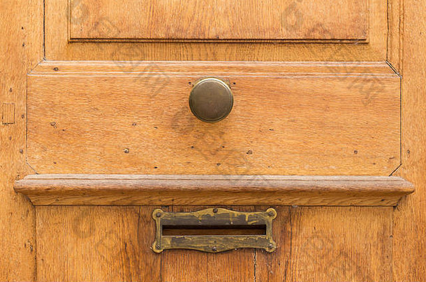 旧的浅棕色木门，带圆形金属把手和邮箱开口。门把手和邮箱的近景。