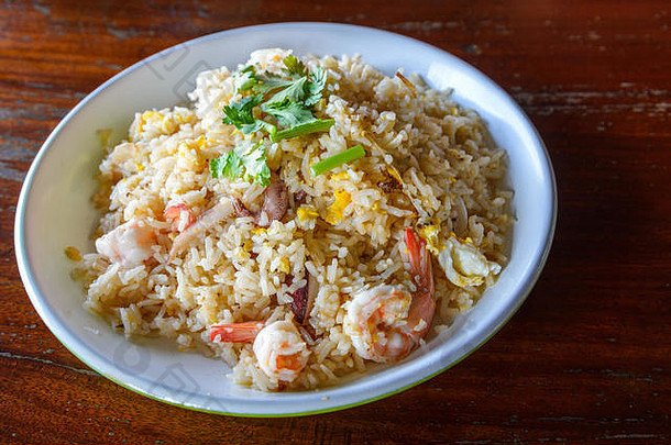 泰国亚洲海鲜炒饭配虾和鱿鱼，白碟和粗桌。