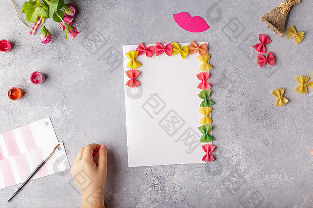 母亲节、3月8日或生日的纸工艺品。小孩正在用彩色纸和彩色面食做一束花。