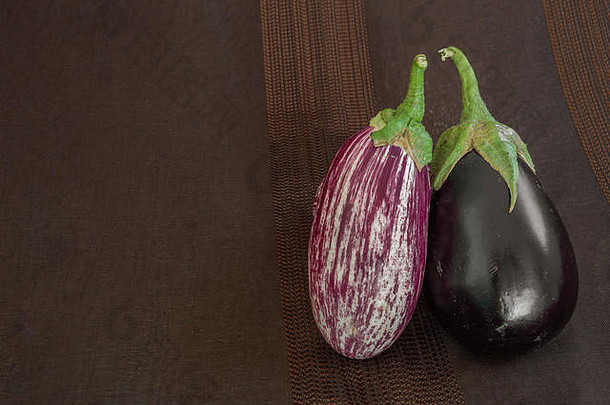 深色织物背景上有两种不同类型的茄子：普通黑色品种和刮花品种。左侧的空间。