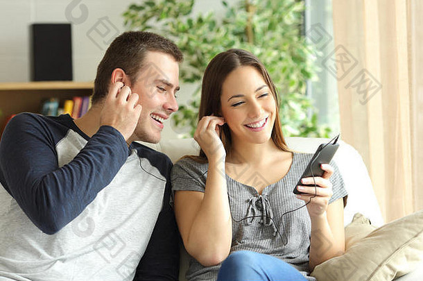 一对幸福的夫妇坐在客厅的沙发上听<strong>音</strong>乐，共享耳机
