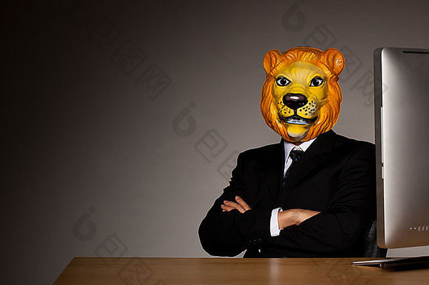穿着西装、戴着狮子面具的男子坐在办公桌旁，手里拿着电脑