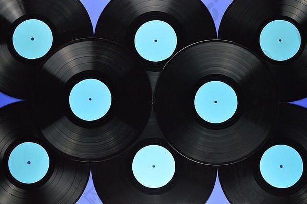 一堆旧的黑色乙烯基唱片，蓝色背景上有空白的青色标签