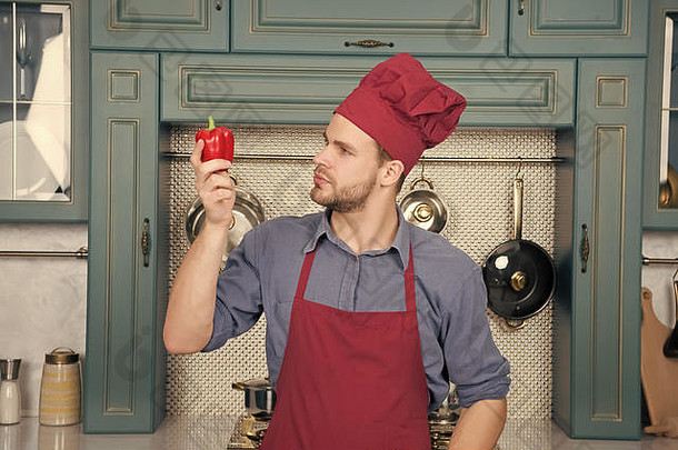 厨师戴着红帽子，围裙上围着蔬菜。厨师看着厨房里的甜椒。素食者，健康，饮食，维生素。食物，烹饪，菜肴，<strong>菜单菜谱</strong>