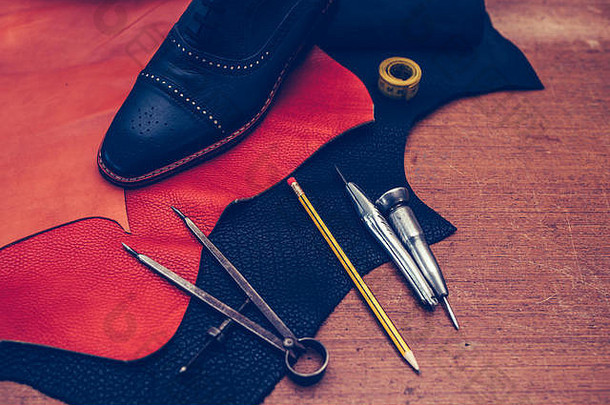 鞋匠的办公桌。鞋匠工作场所的工具和皮革。男士经典黑皮鞋、皮革制鞋工具及成套皮革工艺工具。鞋