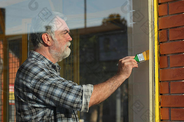 成年男子将金属窗漆成黄色，旧店铺窗户翻新