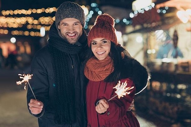 在公园举行的圣诞节庆祝活动上，一对<strong>美</strong>丽的夫妇穿着暖和的外套、针织帽子和围巾，在<strong>户外新年</strong>派对上手持魔法火花