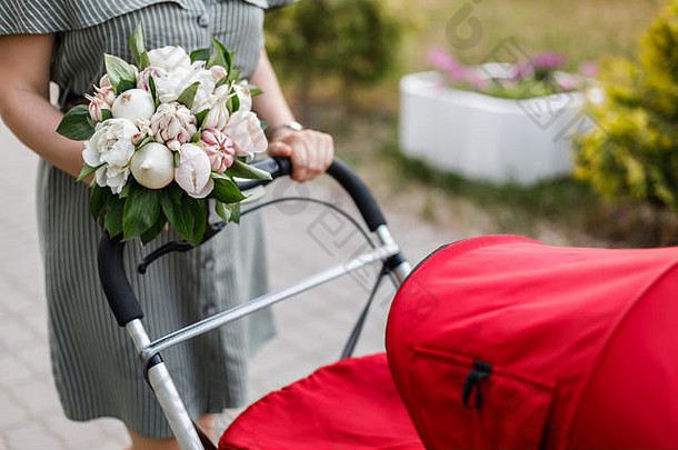 年轻的母亲提着一辆红色的婴儿车走着，手里拿着一束<strong>原汁原味</strong>的鲜花、洋葱和大蒜